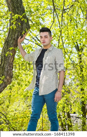 A young handsome guy is standing by a tree in the morning of a spring season. / Portrait of Young Guy