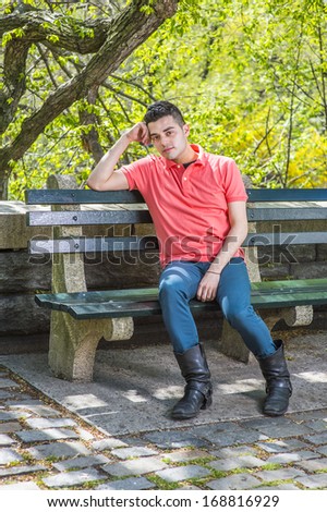 Dressing in a red Polo shirt, green pants and long leather boots, one arm supporting his head, a young handsome guy is sitting on a long chair  in the morning of a spring season, relaxing