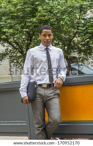Dressing in white shirt, a black tie, gray pants, carrying a briefcase, a young handsome black college student is standing on a campus, smilingly looking at you. / Portrait of a College Student