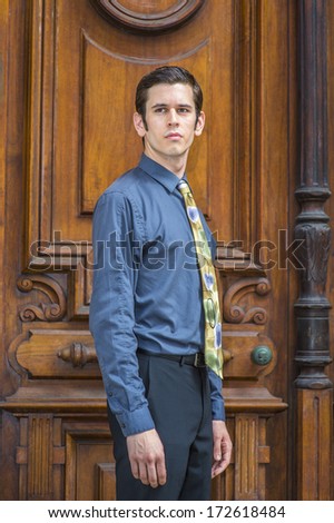 Dressing in a blue shirt, pants and a colorful tie, a young college student is standing in the front of old fashion style office door, looking forward. / Portrait of College Student