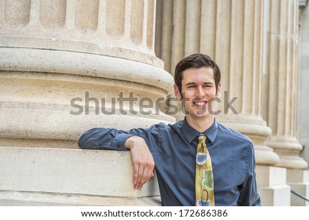 Dressing in a blue shirt, a colorful tie, a young college student is standing outside an office building, smiling and relaxing / Portrait of College Student