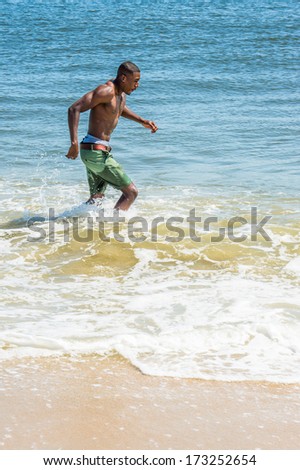 Waving arms, a well built young sexy black guy, half naked,  is running on water of ocean. / Running on Water