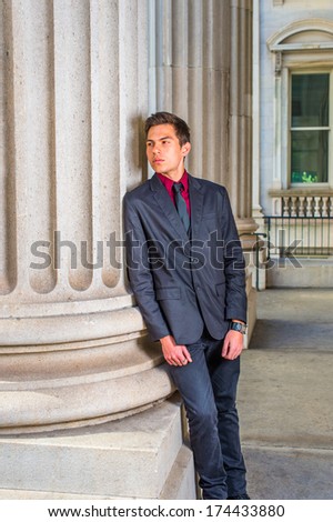 Dressing in a red undershirt, a black blazer, black jeans and a black tie, a college student is leaning against a column outside an office on the campus, relaxing and thinking. / Relaxing Outside