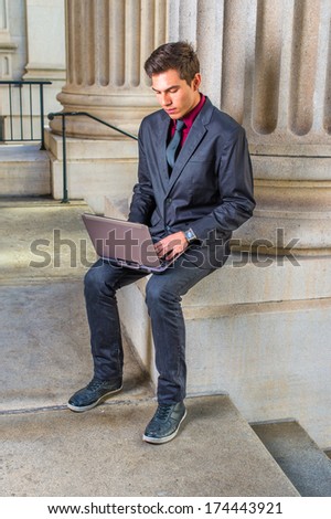 Dressing in a red undershirt, a black blazer, jeans, a black tie, a young college student is working on a laptop computer outside an office on campus. / Studying Outside
