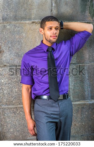 Dressing in a purple shirt, gray pants, a black tie, one hand putting in the back of his head, a young college student with a little beard and mustache is leaning against the wall,  thinking outside.