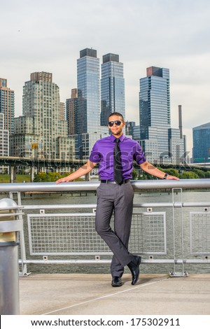Dressing in a purple shirt, gray pants, a black tie, leather shoes, wearing a sunglasses, a young businessman with a little beard and mustache is standing outside a busy business district, relaxing.