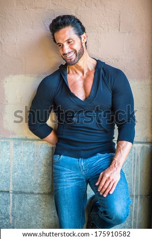 Dressing in a black sweater and blue jeans, a handsome, sexy, middle age guy with mustache and beard is leaning against the wall, looking down, smiling, lost in thought. / Day Dream