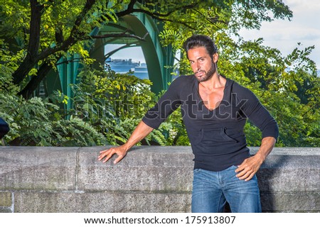 Dressing in a black sweater and blue jeans, a handsome, sexy, middle age guy with mustache and beard is standing by the half wall of fence, seriously looking at you. / Relaxing Outside