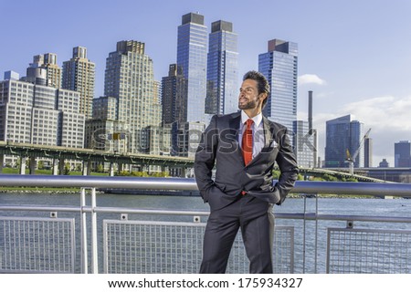 Dressing is a black suit, a red tie, hands in pockets, a sexy, middle age businessman with mustache and beard is standing in the front of a business district, confidently looking forward./Businessman