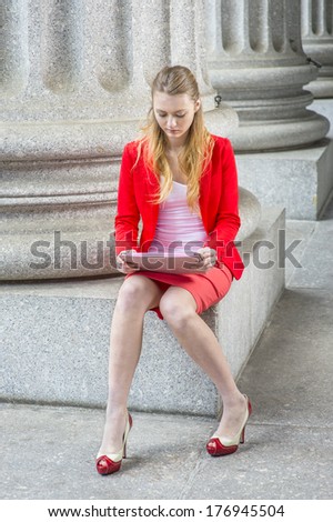 Dressing in a red blazer, white under wear, a red skirt, open toes high heels, a college student is sitting on a column base outside an office, studying on a tablet computer. /Studying Outside