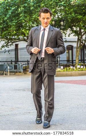Wearing a black striped jacket, pants, tie, leather shoes,  a young businessman is walking outside an office building. / Businessman Walking