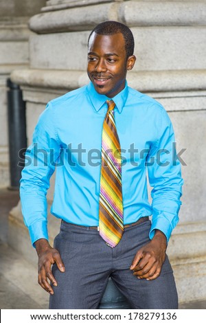 Dressing in a light blue shirt, a colorful pattern tie, a young black businessman is smiling, sitting outside to take a break. / Happy Black Businessman