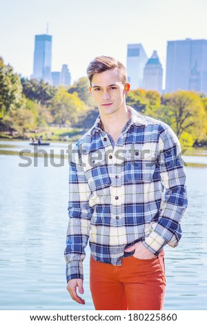 Portrait of Young Man. Dressing in a long sleeve, patterned shirt, red pants, one hand putting in pocket, a young guy is standing by a lake. High business buildings in background. Instagram effect.