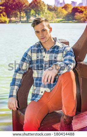 Dressing in a long sleeve, patterned shirt, red pants, one young guy is causally sitting by a lake, relaxing and thinking. Instagram Toaster filter effect. /Young Man Relaxing Outside