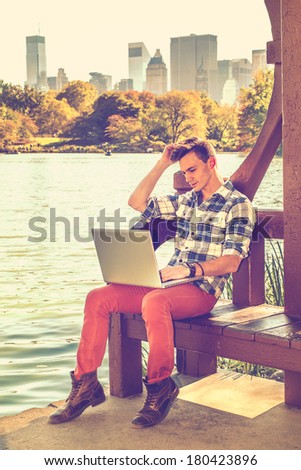 Dressing in a long sleeve, patterned shirt, red pants, brown boots, scratching his head, one young guy is working on a laptop computer by a lake in afternoon. / Student Studying Outside