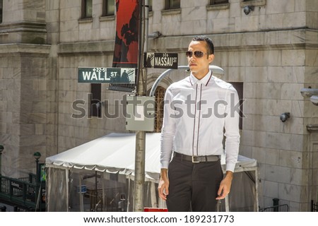 Businessman on Wall Street. Dressing in a white shirt, black pants, wearing sunglasses, a young handsome man is standing on street, confidently looking forward. Wall Street sign in the background.