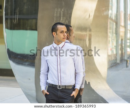 Man with Reflection. Dressing in a white shirt, black pants, two hands putting in pockets, a young handsome guy is standing by a modern mirror wall, passionately waiting for you.
