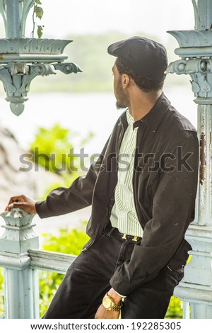Rainy Day, a little foggy, wet feel. Wearing a jacket, unbuttoned, a ivy cap,  a young black man is sitting against a pole inside a pavilion by a lake in a raining day, turning head, looking back.