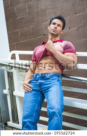 Strong man relaxing outside. Holding on his shirt, showing his strong body, a handsome, sexy, middle age guy is leaning back on railings, looking up, thinking.