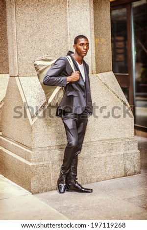 Street Fashion. Wearing a white under wear, fashionable jacket, pants, leather shoes, carrying a shoulder bag,  a young black college student is standing outside an office building, thinking.