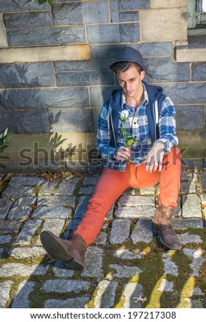 Man Missing you. Dressing in a pattern shirt, a hoodie vest,  jeans, leather boot shoes, wearing a woolen Fedora hat, a young guy is sitting on the ground, holding a white rose, looking at you.
