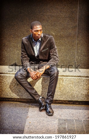 Young black man thinking outside. Dressing in a blazer, pants, leather shoes, a young black guy is sitting on a marble stone bench, into deeply thinking. Street Fashion.