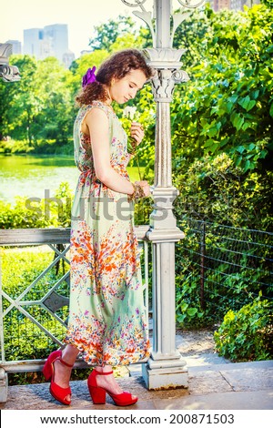 Lady Missing You on Park. Dressing in sleeveless, light green, long dress, red sandals shoes, a pretty teenage girl is standing inside a pavilion, hands holding a white rose, looking down, thinking.