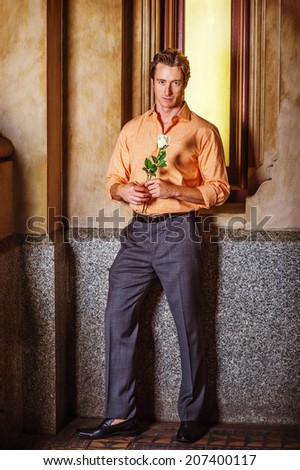 Man waiting for you. Dressing in a light orange patterned shirt, gray pants, leather shoes, hands holding a white rose, a young handsome guy is standing by a small old fashion window, looking at you.