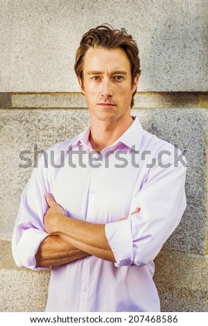 Portrait of Young Man. Wearing a light pink shirt, crossing arms, a young handsome guy is standing against a concrete wall, confidently looking at you.