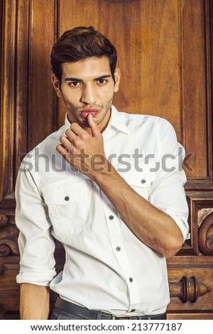 Portrait of Young Businessman. Wearing a white shirt, a young college student is standing by an old fashion style office door, raising a arm, the thumb touching the lip, into deeply thinking.