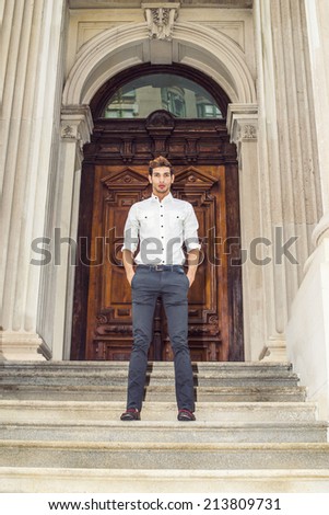 Portrait of Young Businessman. Wearing a white shirt, black pants, leather shoes, hands in pockets, a young handsome guy is standing outside an office building, confidently looking at you.