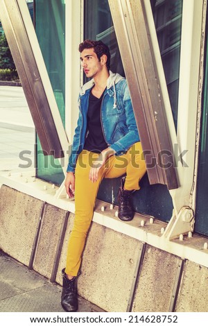 Man Missing You. Dressing in a blue jacket with hood, black under wear, yellow pants, leather boot shoes, a young handsome guy is standing by a metal structure on the corner, looking up, thinking.