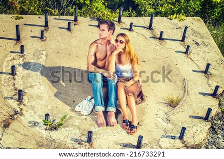 Story Teller. Guy wearing jeans, barefoot, half naked, girl dressing in skirt, tank top,  sunglasses, a young couple is sitting on the concrete slope with rusty metal rods, relaxing, thinking.