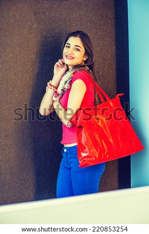 Happy Woman. Wearing red short sleeve shirt, light weight scarf, blue pants, shoulder carrying a red leather shopping bag, a beautiful lady standing in modern interior, smiling, looking at you.