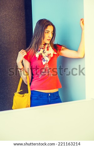 Modern Business Woman. Wearing red short sleeve shirt, light weight scarf, blue pants, arm carrying a yellow leather hand bag, a beautiful lady standing in modern interior, thinking, lost in thought.