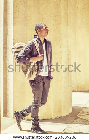 Man Traveling. Carrying a shoulder bag, a young black college student is walking though columns on campus, confidently looking forward. Street Fashion.