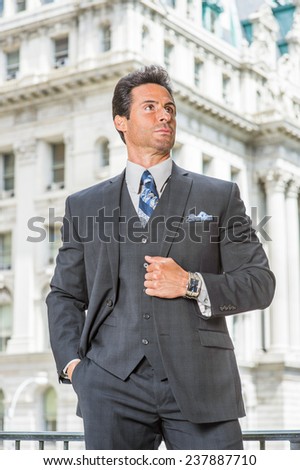 Man Power. Dressing in dark blue three piece suit, necktie, holding a fist, a handsome, sexy, middle age businessman is standing outside office building, confidently looking up.