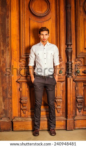 Man Casual Fashion. Wearing a white shirt, black pants, leather shoes, hands in pockets. a young college student is standing by an old fashion style office door, confidently looking at you.