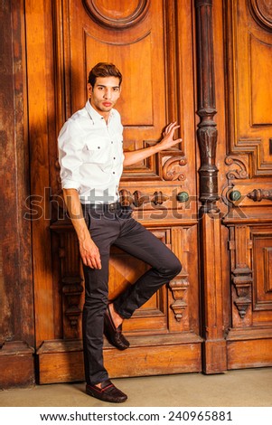 Man Casual Fashion. Wearing a white shirt, black pants, leather shoes, a young college student is standing by an old fashion style office door, a hand touching door, bending a leg, waiting for you.