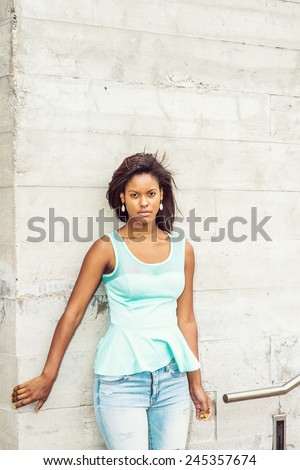 Girl Waiting for you. Wearing a green tank top, drop earrings, blue jeans, a young pretty woman is standing against the wall outside in the wind, waiting for you. Woman casual fashion