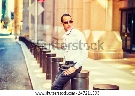Man Relaxing Outside. Dressing in a white shirt, black pants, wearing sunglasses, a young, mysterious guy is sitting on the street outside office building, looking around. Instagram filtered look.