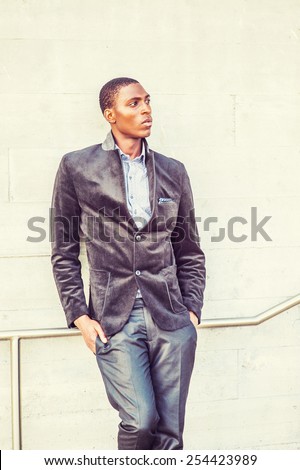 Young black man thinking outside. Wearing a fashionable jacket, a young black college student standing against the wall, looking away, thinking. Concept of teenager self esteem. Retro filtered look.