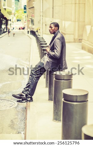 City Life. Young black college student sitting on street, hunchbacked, sad, tired, thinking, lost in thought. Concept of teenagers questioning life, career, self esteem. Retro filtered look.