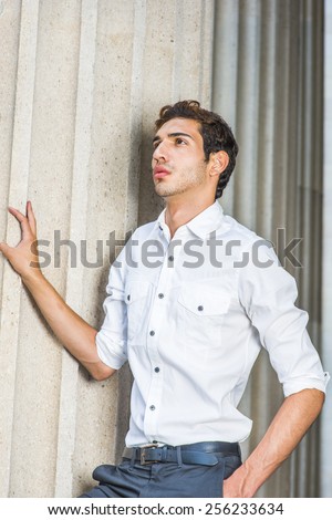 Portrait of Young Professional. Wearing a white shirt, sleeves rolling over, a young college student with a little beard is standing by columns on campus, thinking, confidently looking up.