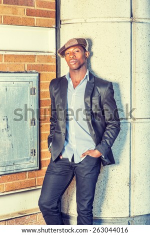Portrait of Young Black Guy.  Wearing fashionable Newsboy cap, black blazer, unbuttoned,  a young guy is standing on the corner of the street, looking at you. Man Urban Fashion. Instagram effect.