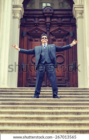 Dressing in three pieces suit, necktie, vest, leather shoes, wearing sunglasses, a handsome, middle age businessman stand in front of vintage style office door way, stretch arms, excited by success.