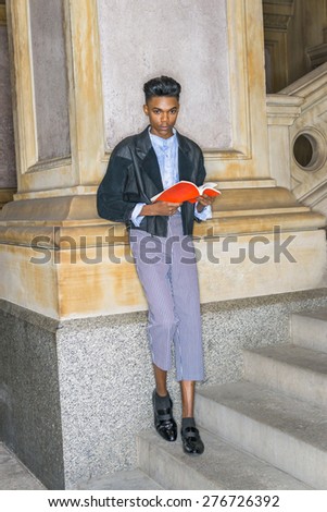 A young,18 years old student, wearing black jacket, striped pants, leather shoes, standing on stairs, leaning against column on campus, hands holding red book, reading, looking up, waiting for you.