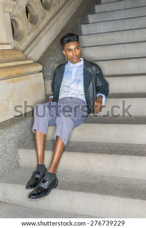Teenage Casual Fashion. A young dark skin,18 years old student, wearing black fashionable leather, wool mixed jacket, striped pants, blue dyed white shirt, leather shoes, sitting on stairs, relaxing.