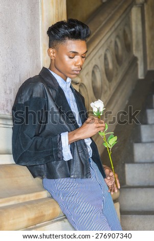 Boy with white rose.  A young,18 years old student, wearing black fashionable leather, wool mixed jacket, striped pants, hands holding flower, waiting for you in downstairs, thinking, lost in thought.