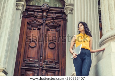 Modern East Indian American Business Woman. Wearing sleeveless orange shirt, arm carrying laptop computer, a young college student standing outside vintage style office building on campus, looking up. Сток-фото © 